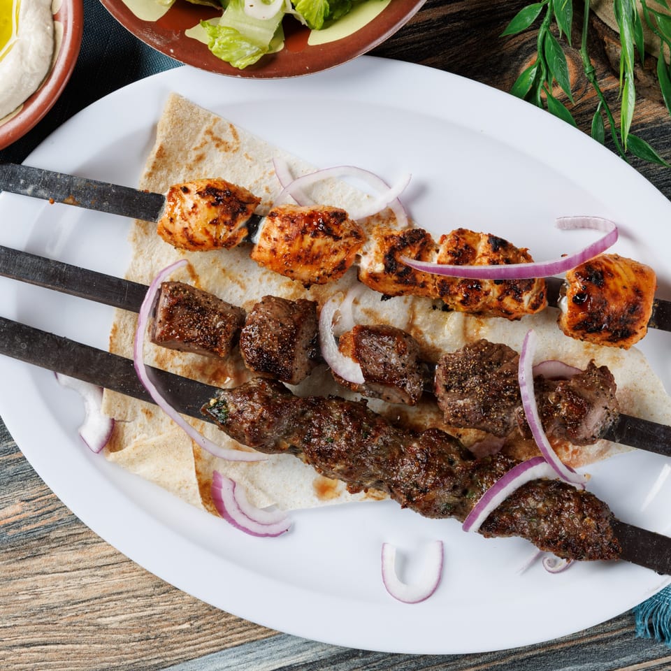 Three skewers of grilled REEF KABOB, two with chicken and one with beef, on flatbread with red onions.
