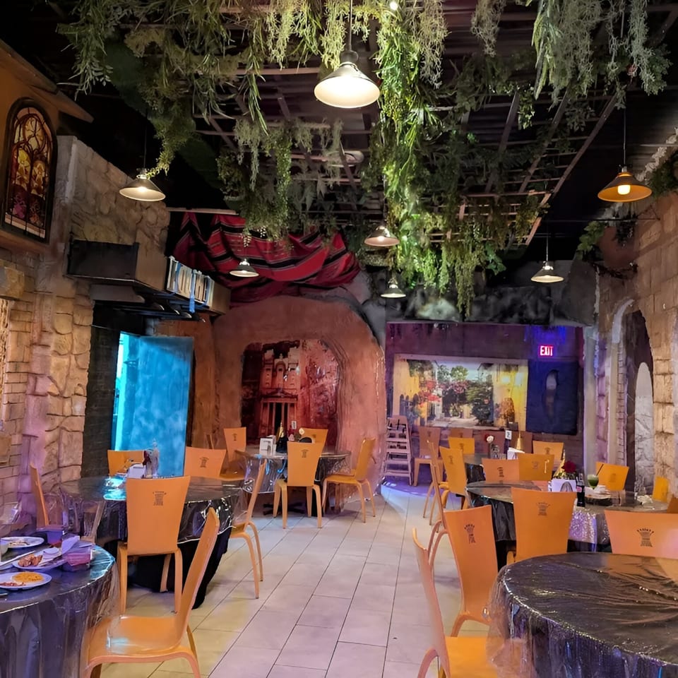 The REEF KABOB dining room features orange chairs, black tables, and hanging greenery under warm lighting.