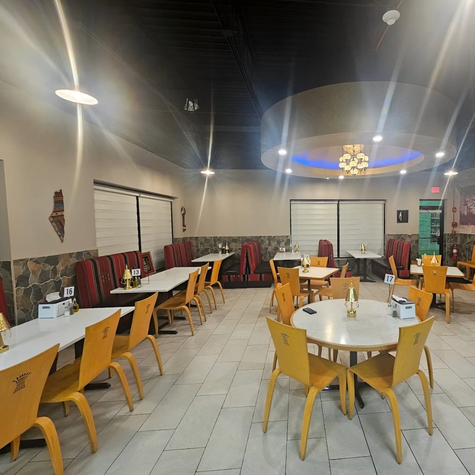 Interior of REEF KABOB restaurant with yellow chairs, white tables, and red-striped booth seating.