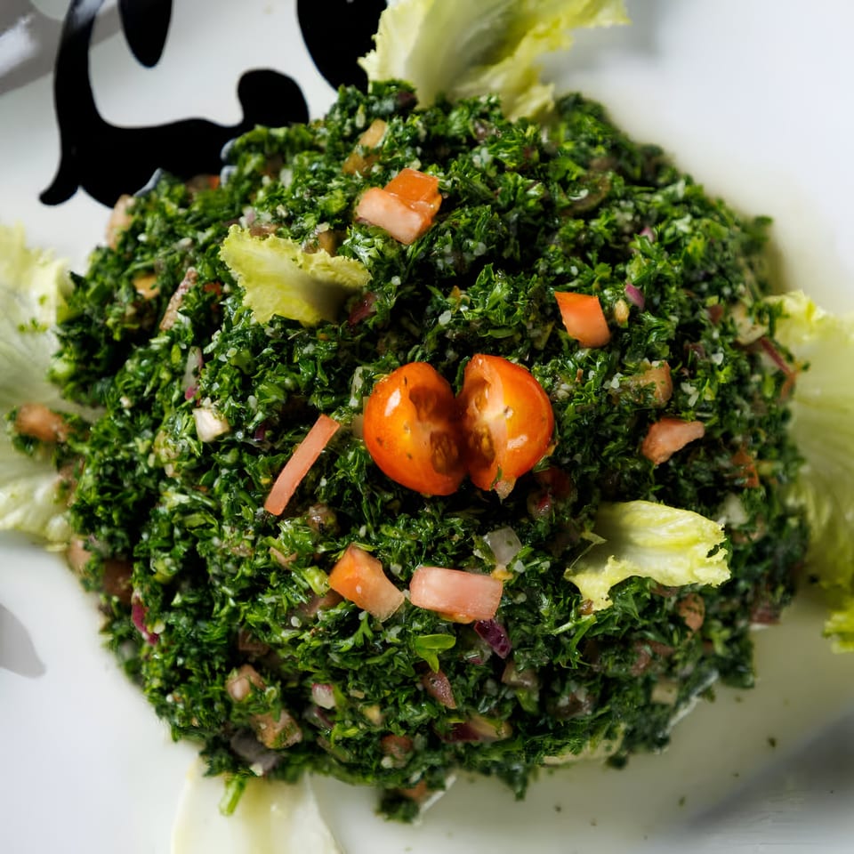 Close-up of a vibrant green tabbouleh salad with chopped tomatoes and lettuce on a white plate.