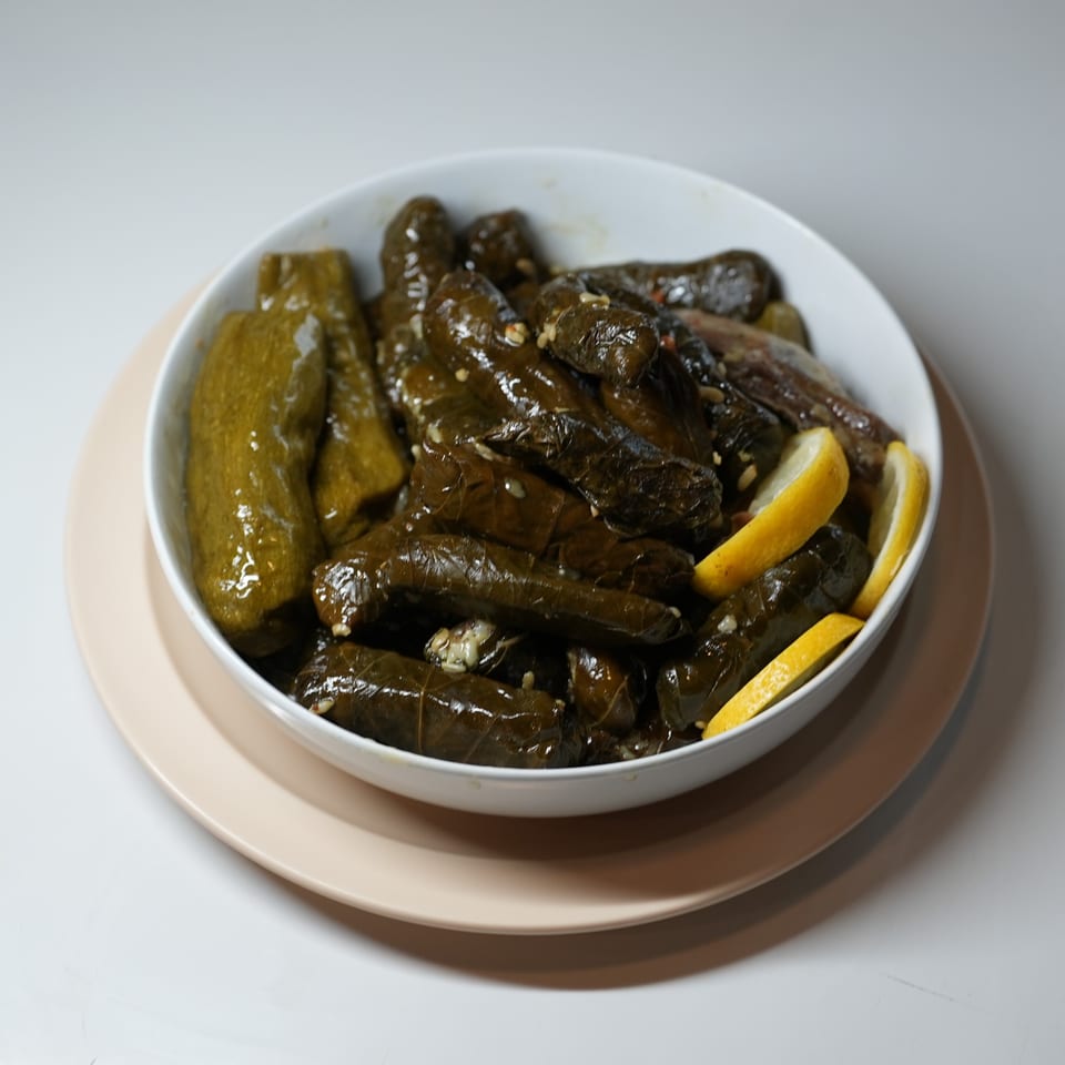 A white bowl filled with stuffed grape leaves and zucchini, garnished with lemon slices.