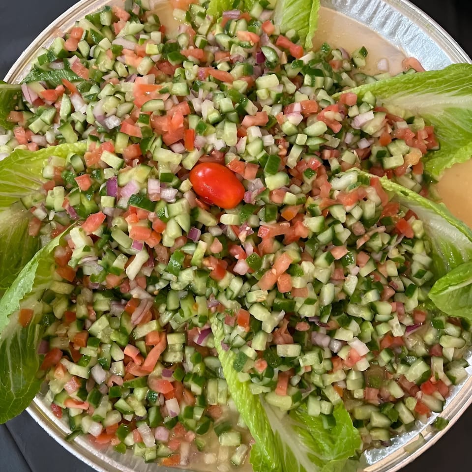 Diced cucumber, tomato, and onion salad, garnished with lettuce leaves and a single grape tomato.