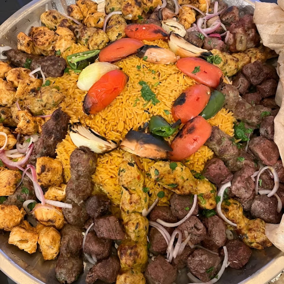 A large platter of REEF KABOB's Middle Eastern grilled meats, rice, and vegetables.