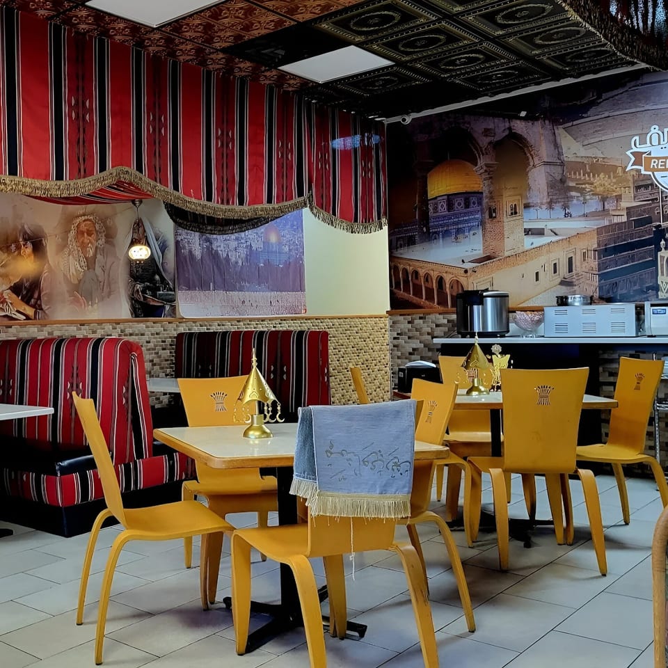 Interior of REEF KABOB restaurant with yellow chairs, red and black striped booths, and Middle Eastern-themed decor.